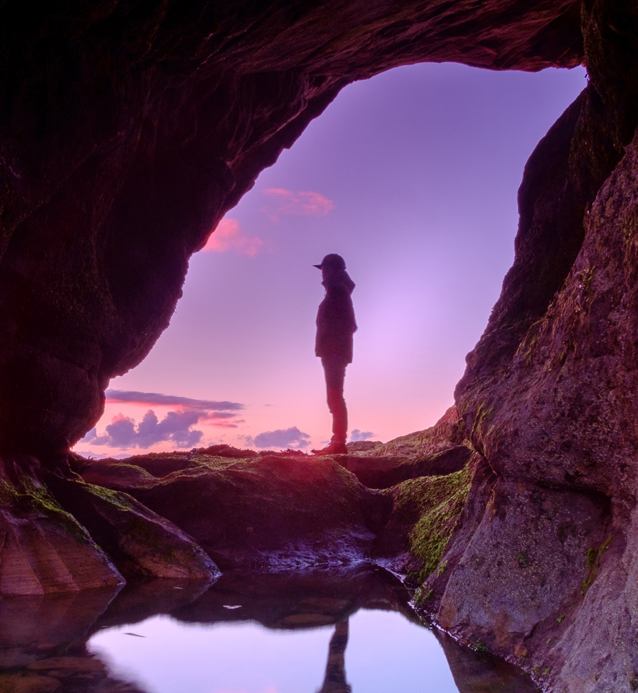 Man standing outside of a cave, looking out to the sky